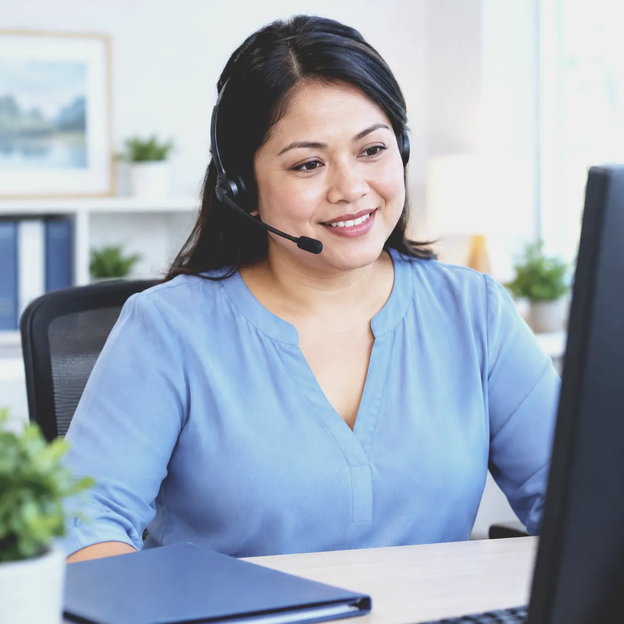 An intake coordinator in a headset smiles at her computer screen